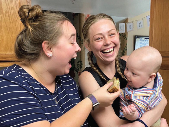 Image of mom holding a baby and AmeriCorps member playing with baby